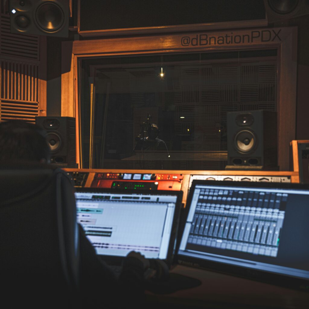 Back view of crop anonymous sound man creating musical arrangement for song while working on desktop computers with track on screen in recording studio